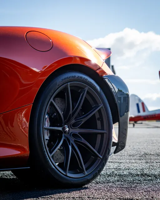 Low-angle detail of an orange McLaren with a vintage aircraft behind