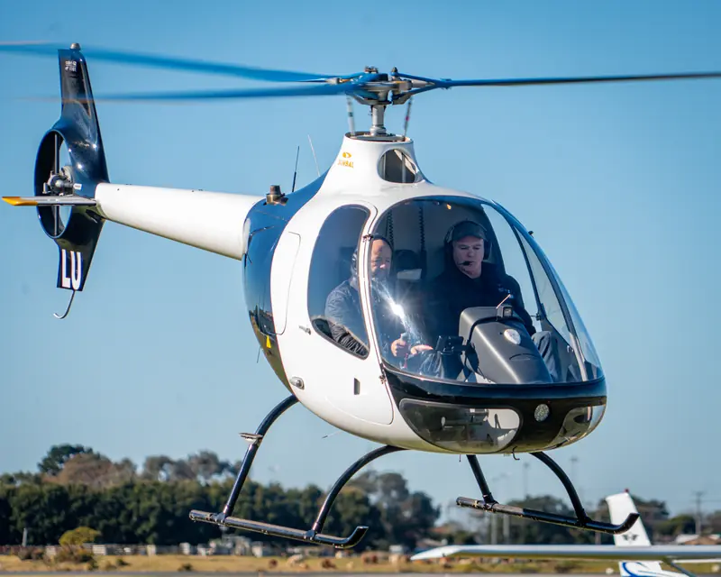 Blue and white light helicopter in flight against a clear blue sky