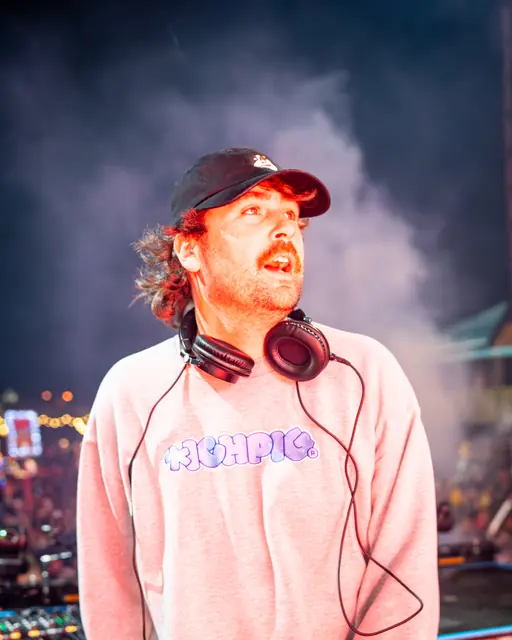 DJ wearing a cap and headphones performing with stage smoke behind