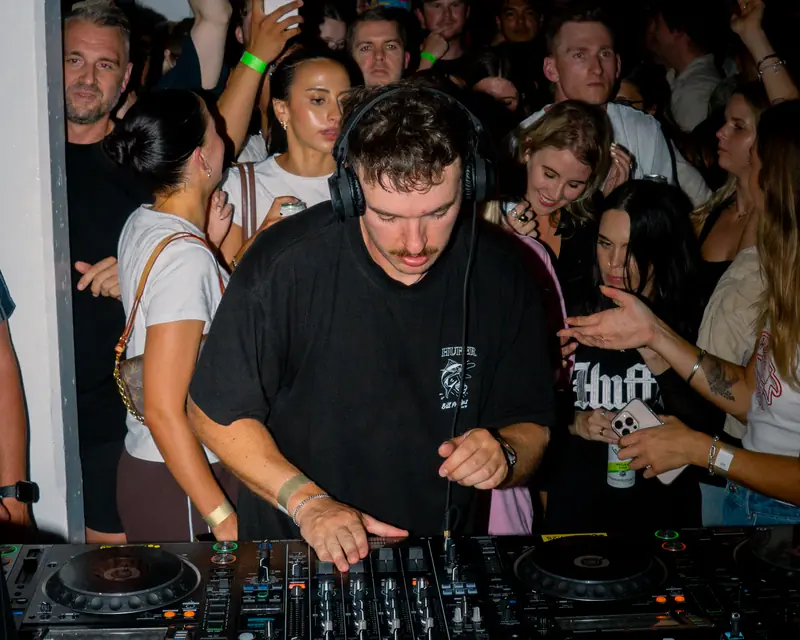 DJ focused on the mixer with an audience gathered close behind