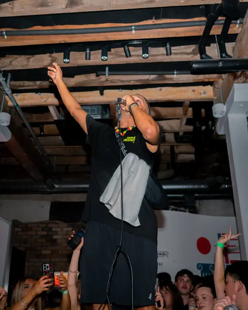 DJ reaching upward beneath the exposed ceiling of a venue